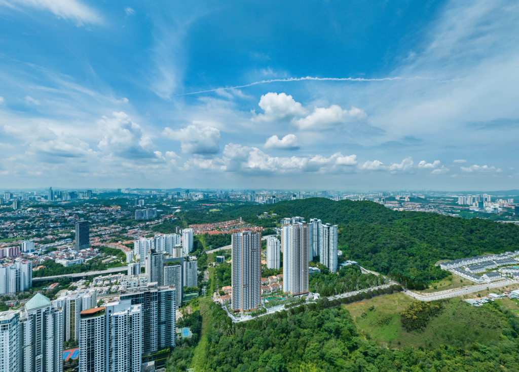 Aerial view of modern high-rise apartment buildings surrounded by green hills, urban skyline, and blue sky with clouds.