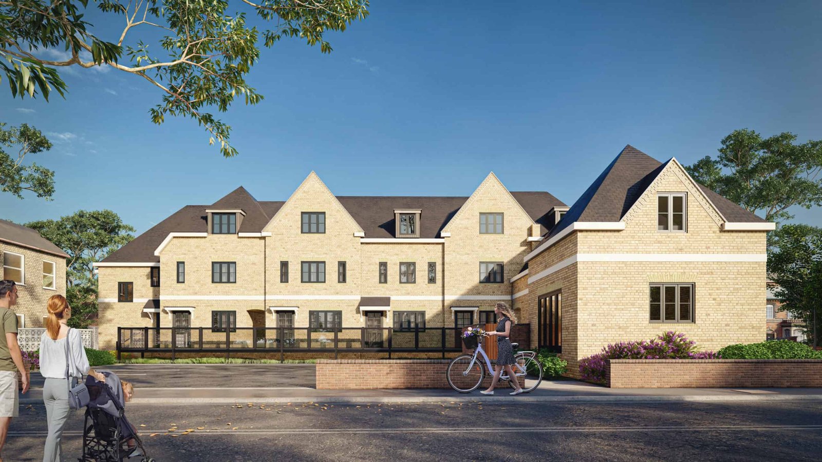 Large beige brick residential building with multiple gabled roofs, landscaped frontage, and people walking and cycling along the sidewalk on a sunny day.