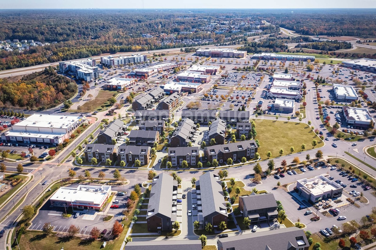 High-angle aerial view of a mixed-use commercial and residential district with multiple buildings, large parking areas, retail spaces, and surrounding road networks. – 3D visualization by Yantram Studio