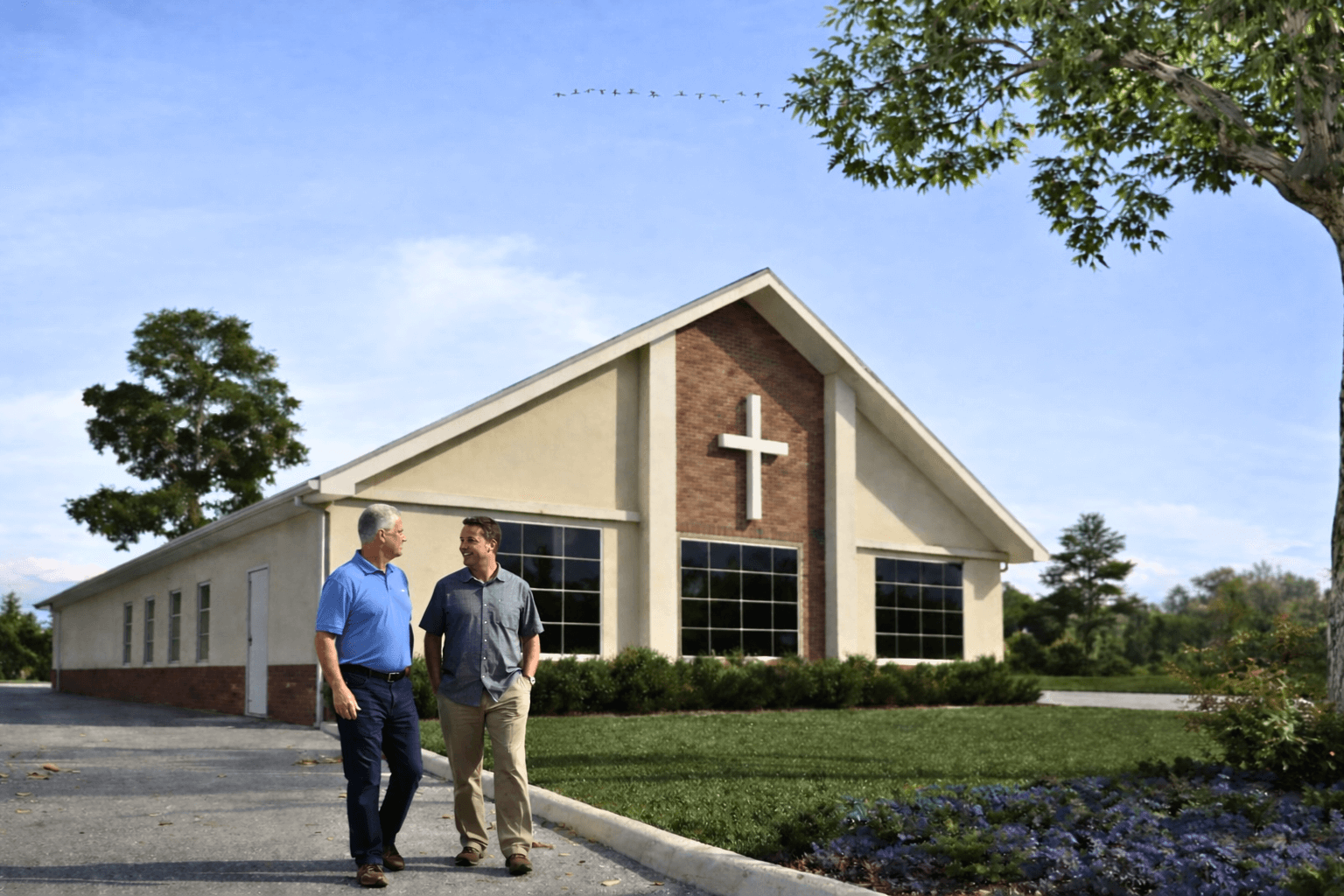 Modern church building with distinctive peaked roof and people standing in forecourt