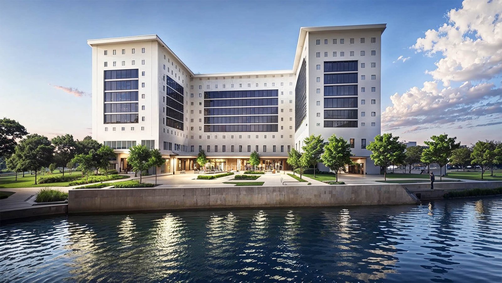 Modern multi-story institutional building with symmetrical façade, large horizontal glass bands, landscaped plaza, and waterfront setting.