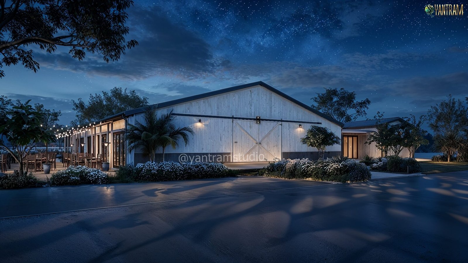 Contemporary barn-style commercial building at night with warm exterior lighting, landscaped greenery, outdoor seating area, and starry sky backdrop.